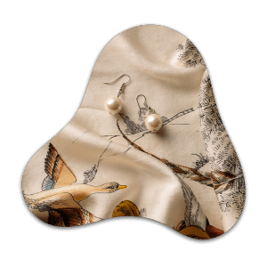 Silky beige fabric featuring a printed bird illustration, styled with pearl earrings.